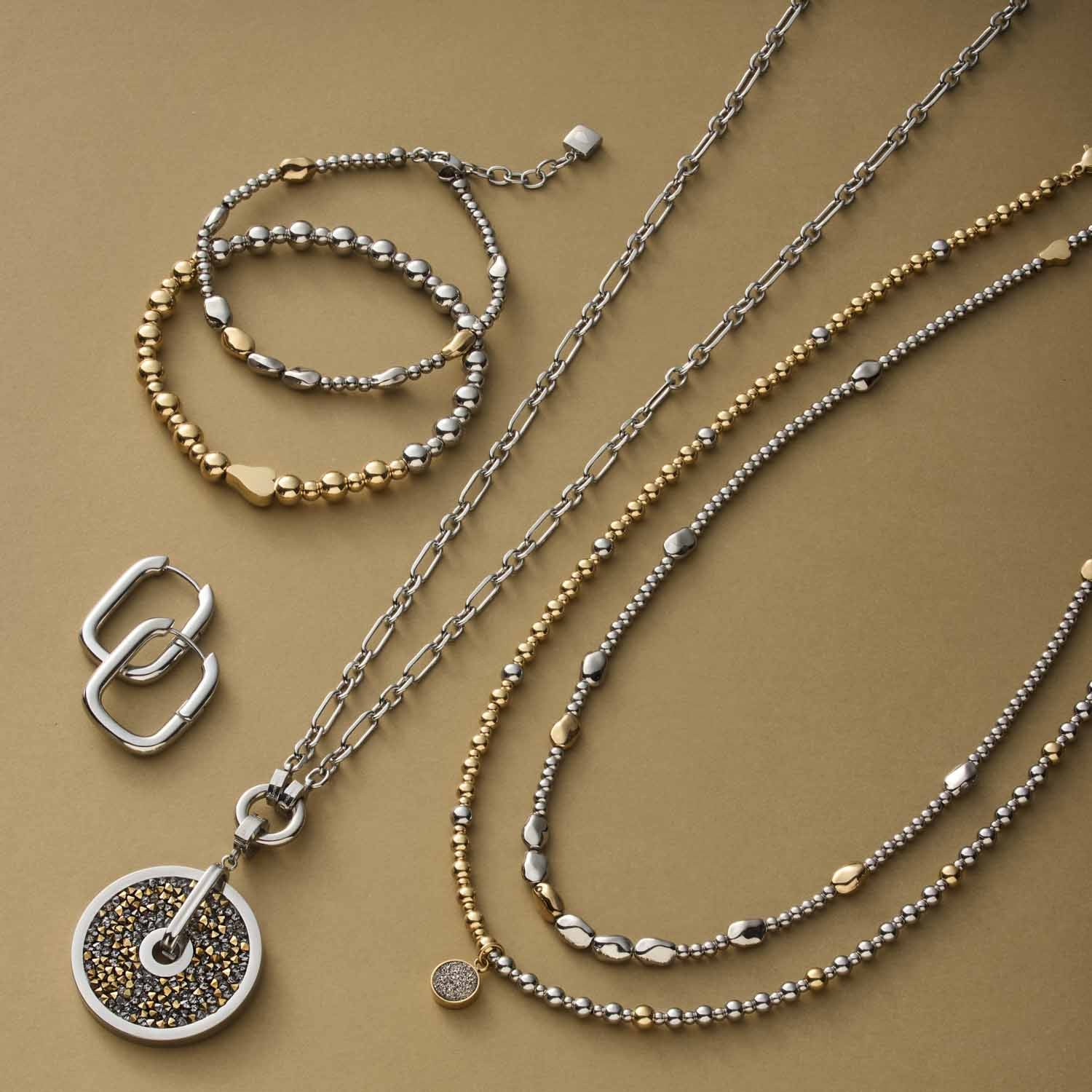 Silberne Schmuckkollektion mit Armbändern, Ketten und Ohrringen auf beigem Untergrund