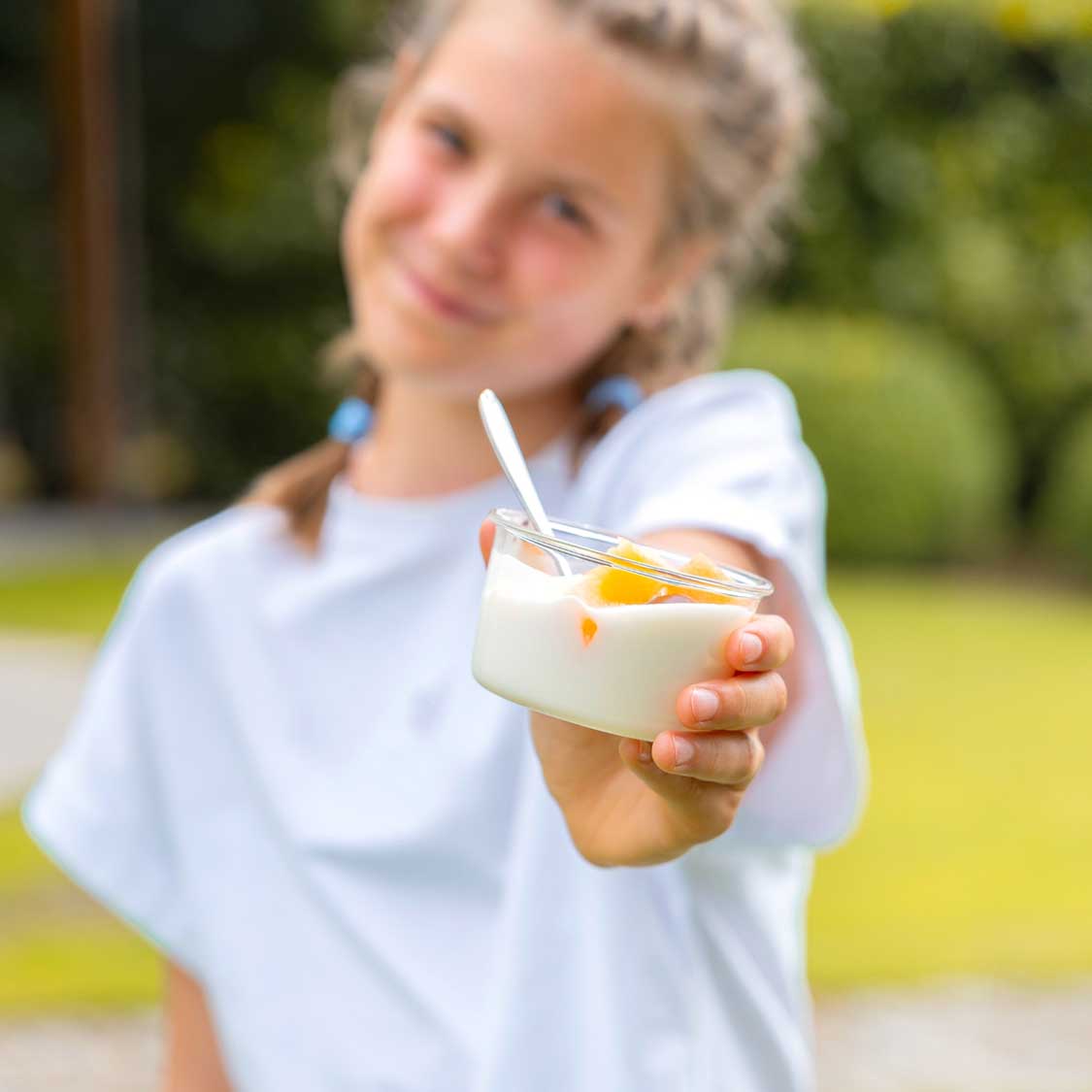 Mädchen hält Glasschale mit Dessert und Eislöffel im Garten