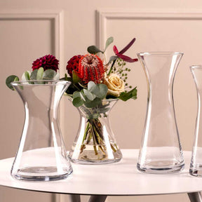 Vase GIA 16 cm mit Blumenarrangement auf weißem Tisch, mehrere klare Glasvasen im Hintergrund