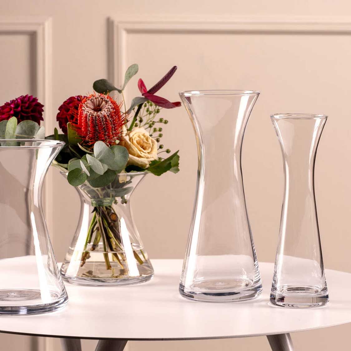 Solifleurvase GIA mit Blumenarrangement auf weißem Tisch, daneben leere Glasvasen