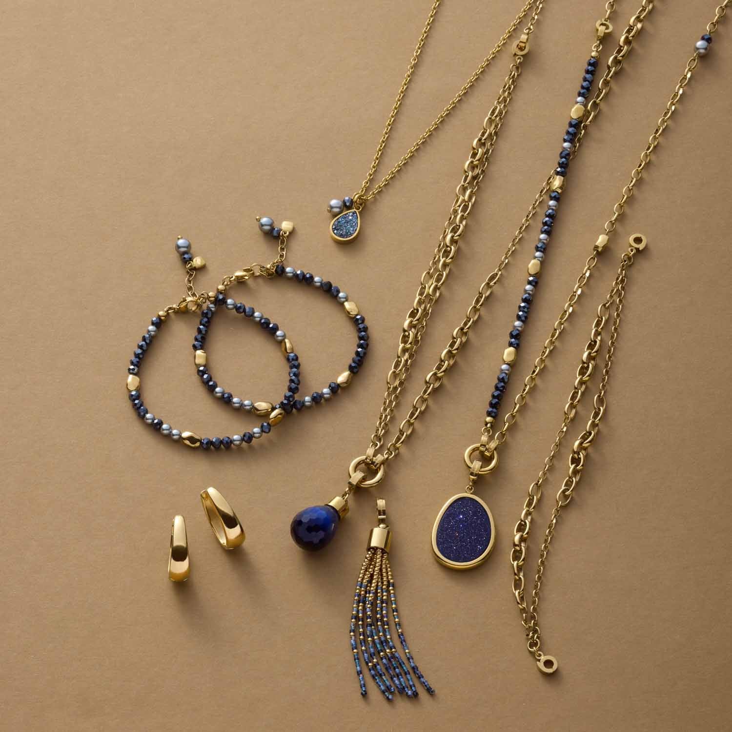 Schmuckkollektion der Serie ALINE mit Armbändern, Ketten und Ohrringen in Gold und Blau auf beigem Hintergrund