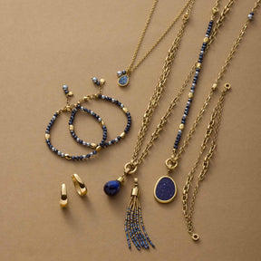 Schmuckkollektion der Serie ALINE mit Armbändern, Ketten und Ohrringen in Gold und Blau auf beigem Hintergrund