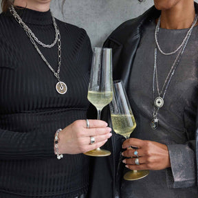 Zwei Personen mit Champagnergläsern tragen silberne Halsketten SINA mit Anhängern