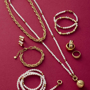 Halskette SINA mit Perlen und Goldketten, Armbänder und Ringe auf rosa Hintergrund