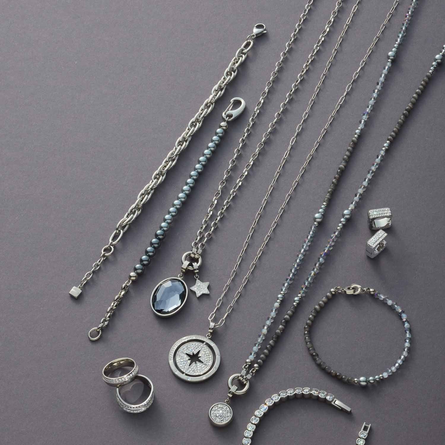 Silberne Schmuckkollektion mit Armbändern, Ketten und Ringen auf grauem Untergrund