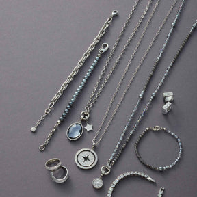 Silberne Schmuckkollektion mit Armbändern, Ketten und Ringen auf grauem Untergrund