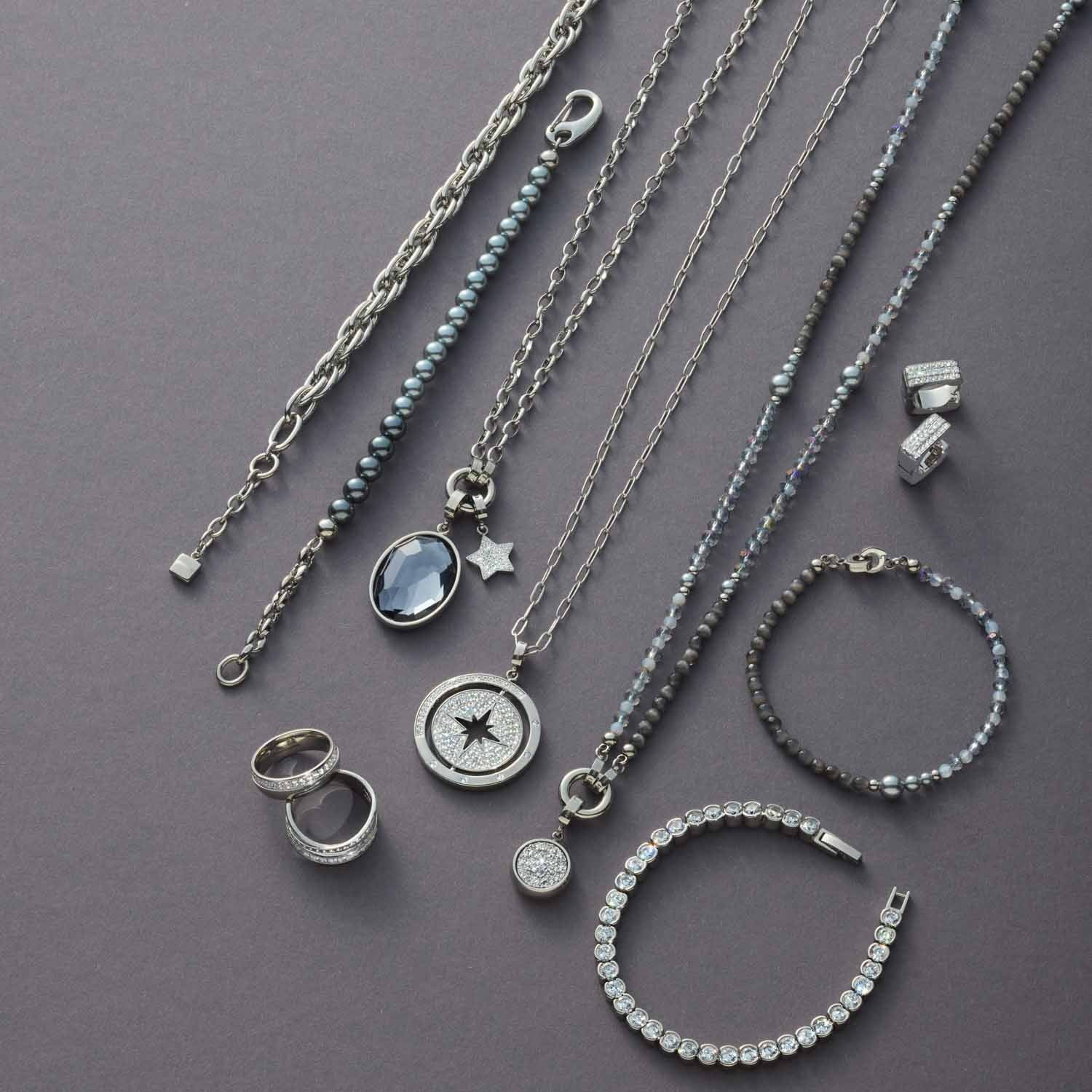 Silberner Schmuck aus der Serie SARAH: Ketten, Creolen, Ringe und Armbänder auf grauem Hintergrund