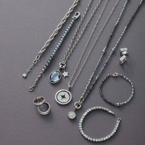 Silberner Schmuck aus der Serie SARAH: Ketten, Creolen, Ringe und Armbänder auf grauem Hintergrund