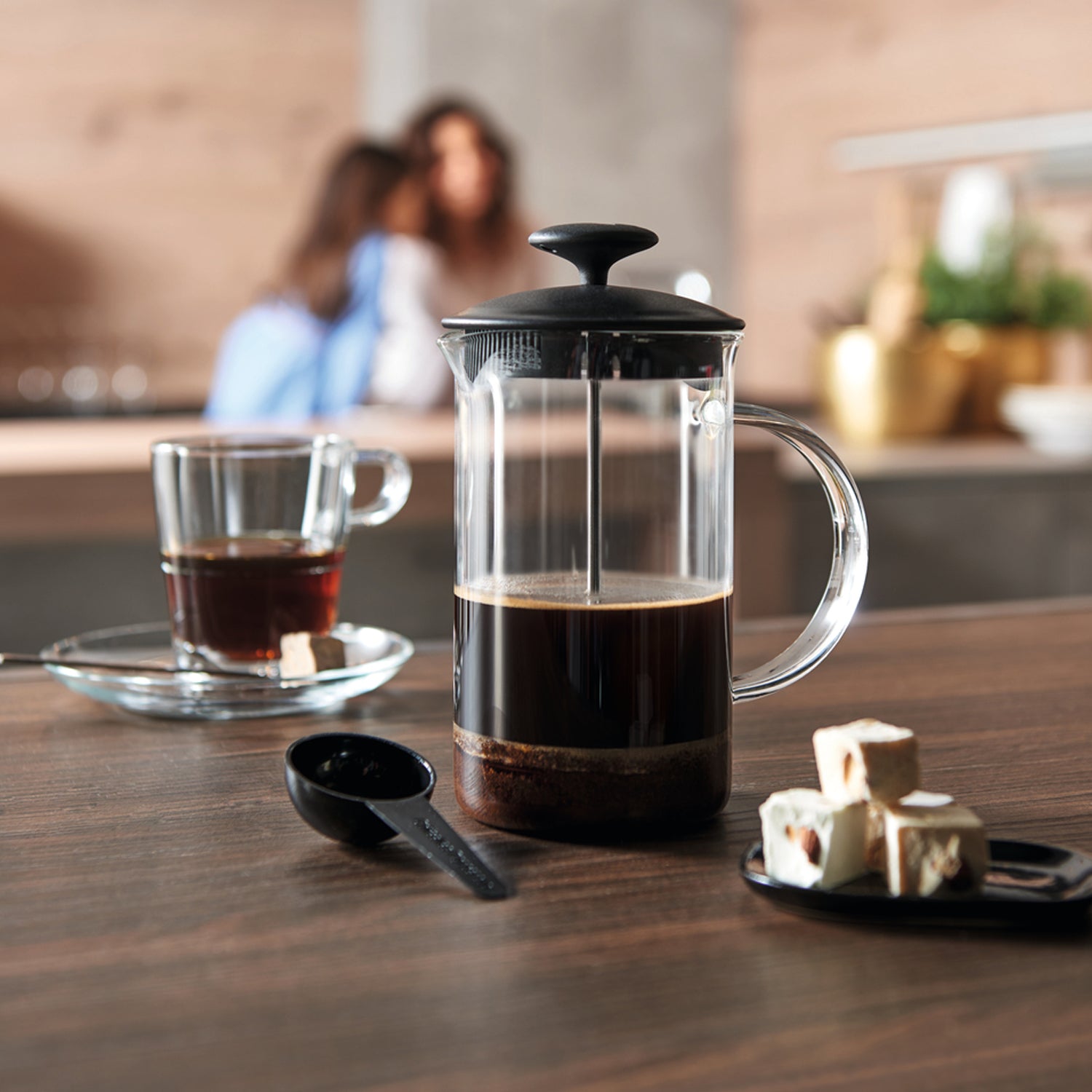 Kaffeebereiter CAFFEE PER ME auf Holztisch mit Kaffeetasse und Zuckerwürfeln, Küche im Hintergrund