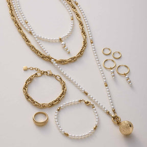 Goldene Ketten, Perlenarmbänder und Ringe in Flatlay-Anordnung auf hellem Untergrund