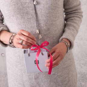 Frau in Strickpullover hält verpacktes Geschenk mit pinker Schleife
