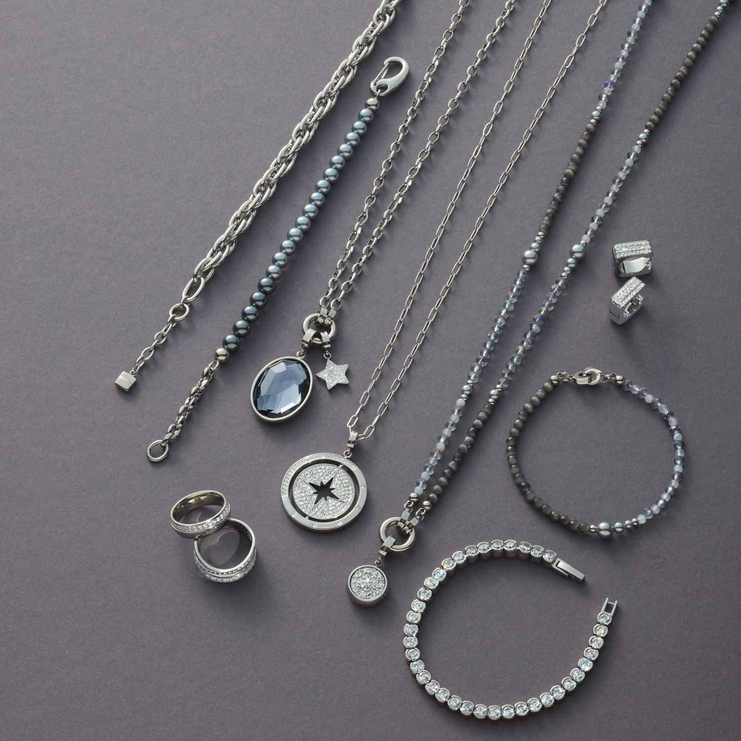 Schmuckkollektion mit Halsketten, Ringen und Armbändern aus Edelstahl auf grauem Untergrund