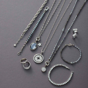 Schmuckkollektion mit Halsketten, Ringen und Armbändern aus Edelstahl auf grauem Untergrund