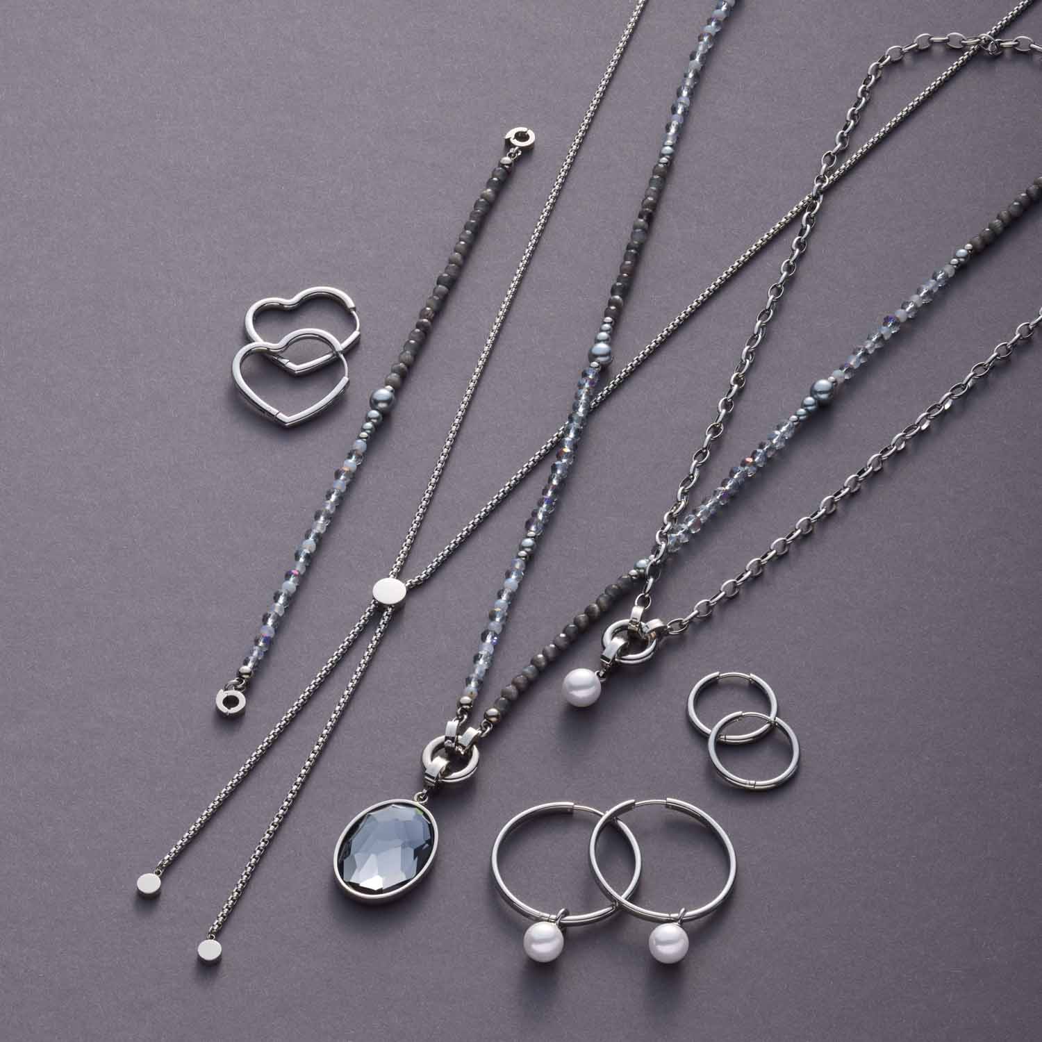 Schmuckkollektion mit Armbändern, Ketten und Ringen aus Edelstahl auf grauem Hintergrund
