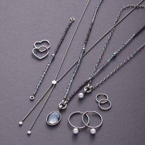Schmuckkollektion mit Armbändern, Ketten und Ringen aus Edelstahl auf grauem Hintergrund
