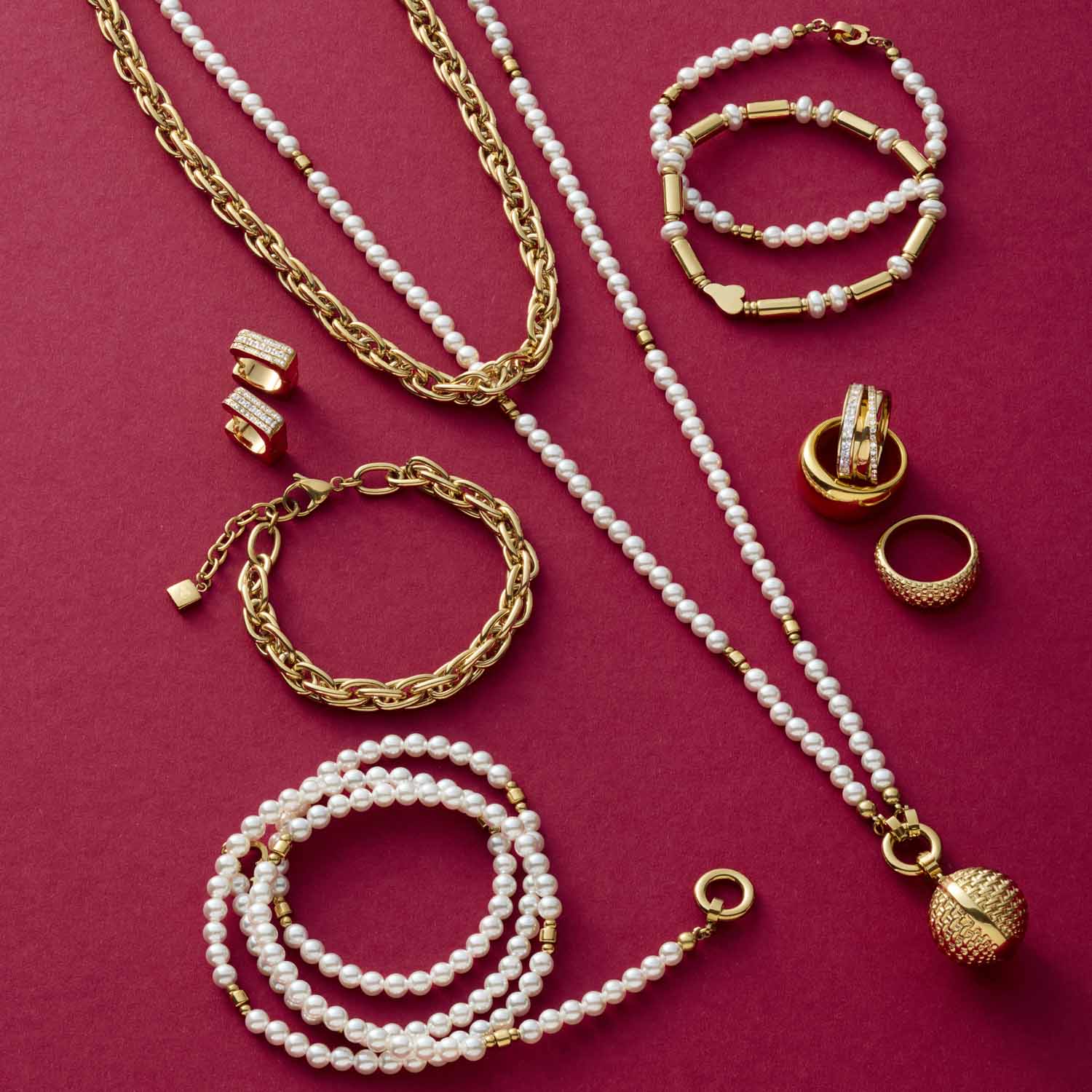 Schmuckkollektion mit goldenen Ketten, Ringen und Perlenbändern auf rosa Hintergrund
