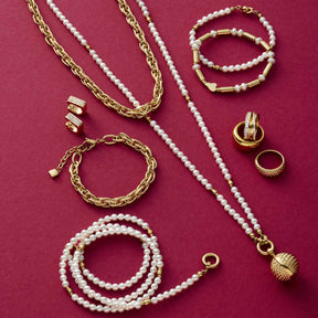 Schmuckkollektion mit goldenen Ketten, Ringen und Perlenbändern auf rosa Hintergrund