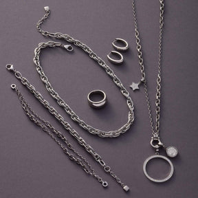 Halskette SUZANNE mit Ketten, Ringen und Anhängern in Silber auf grauem Untergrund