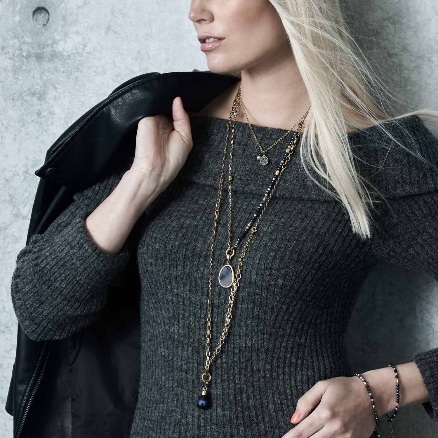Frau trägt grauen Pullover mit goldenem Armband und Halskette, schwarze Jacke