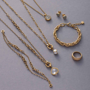 Goldene Schmuckstücke der Serie CLIP&MIX auf grauem Hintergrund, mehrere Ketten, Armband SUZANNE, Ringe und Ohrringe