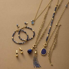 Goldene Schmuckkollektion mit Armbändern, Ketten, Ohrringen und blauen Steinen auf beigem Hintergrund