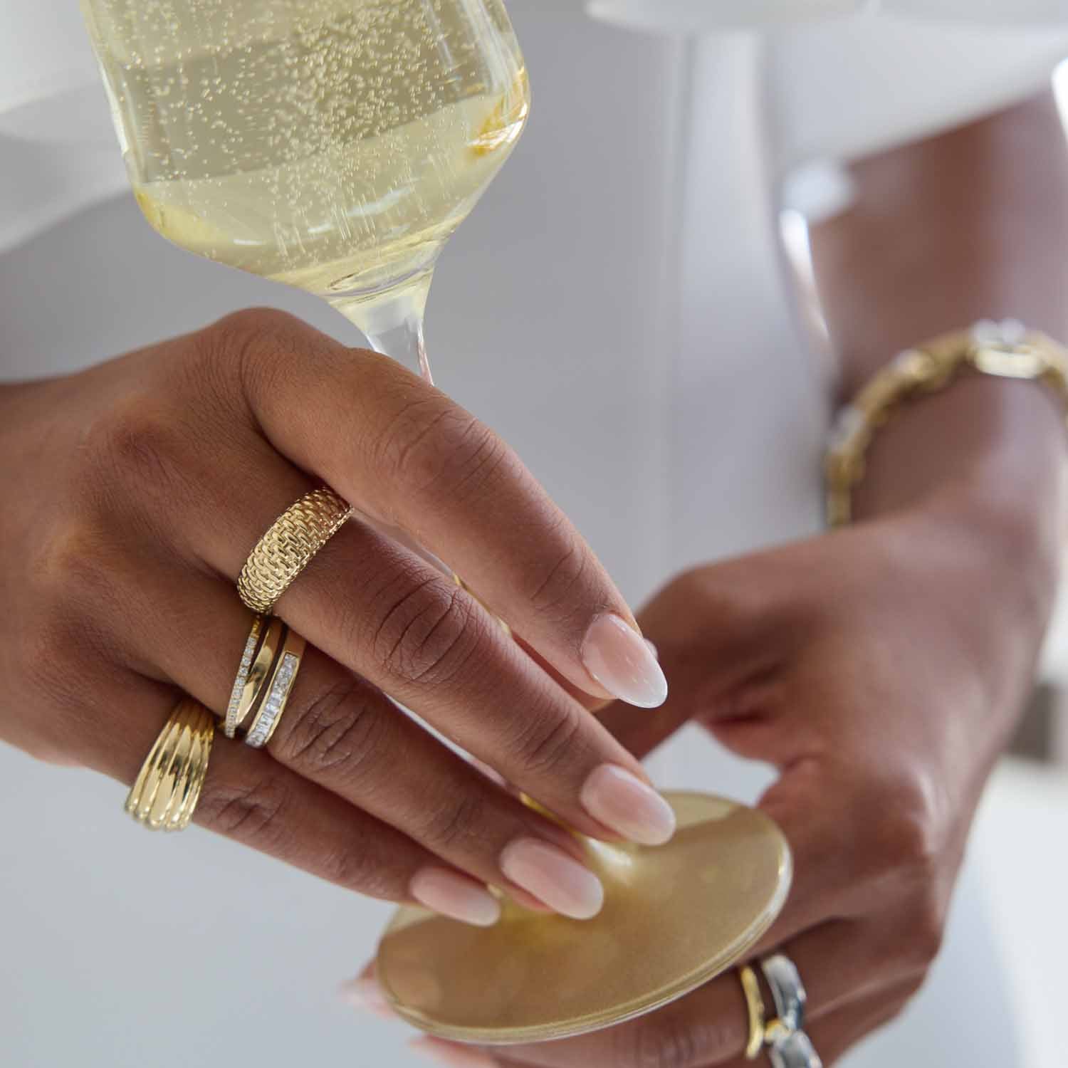 Hand mit goldenen Ringen hält Sektglas, Champagner im Glas