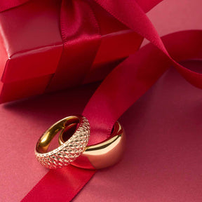Ring PINOU 21 gold auf rotem Geschenkband und rosafarbenem Hintergrund