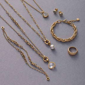 Goldene Kettenhalsketten mit verschiedenen Anhängern und Schmuckaccessoires auf grauem Untergrund arrangiert