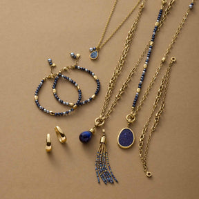 Schmuckset mit Anhängern, Ketten und Armbändern in Gold und Blau auf beigem Untergrund
