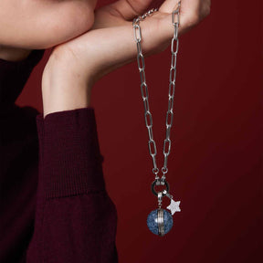 Anhänger SNOWBALL BLUE Clip & Mix an Kette, von Hand gehalten vor rotem Hintergrund