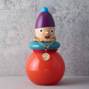 Bunte Holzfigur mit purpurner Kappe, türkisem Kragen und rotem Körper, trägt goldene Kette mit Anhänger