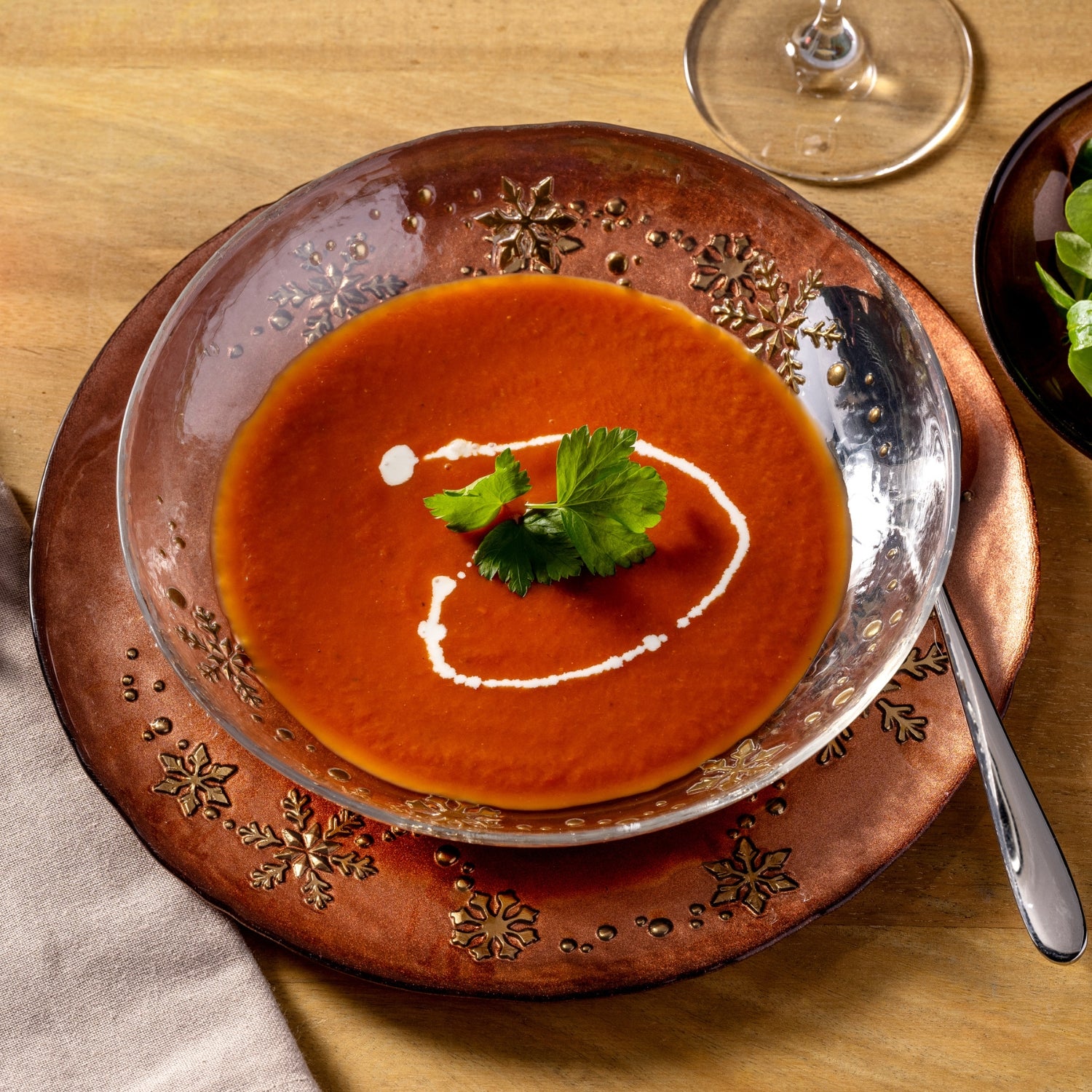 Rote Tomatensuppe in Glasteller auf Holzuntersetzer, Tischgedeck