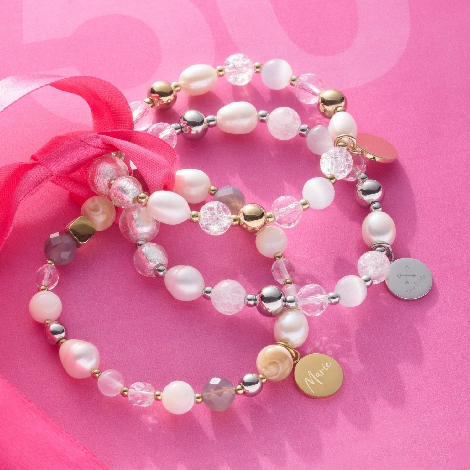 Armband HOPE mit Glasperlen, Metallperlen und gravierten Anhängern auf rosa Untergrund mit pink Schleife