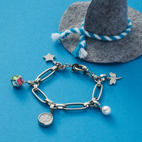 Anhänger ETOILE Clip & Mix an Edelstahlarmband mit weiteren Charms auf blauem Untergrund neben grauem Hut