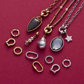 Edelstahlring LOTTI Clip & Mix mit Halsketten und Charms auf pinkfarbenem Hintergrund