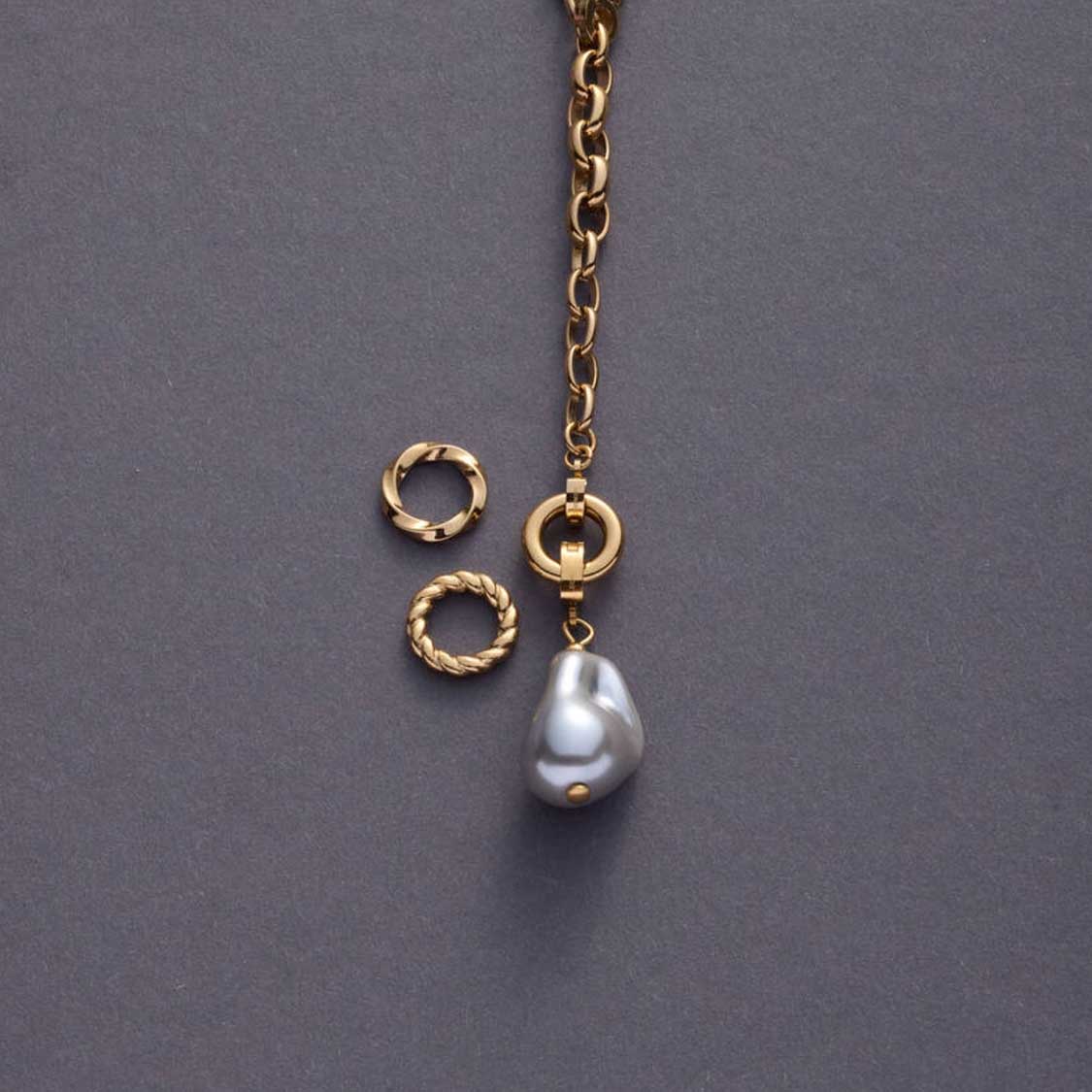 Goldene Kette mit Edelstahlring, austauschbaren Ringen und Perlenanhänger auf grauem Hintergrund