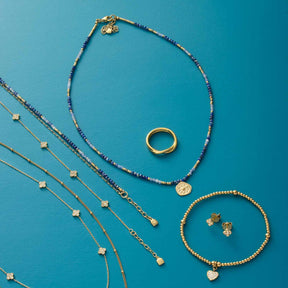 Schmuckkollektion mit Halskette ROSE, Ringen, Armbändern und Ohrringen auf blauem Hintergrund