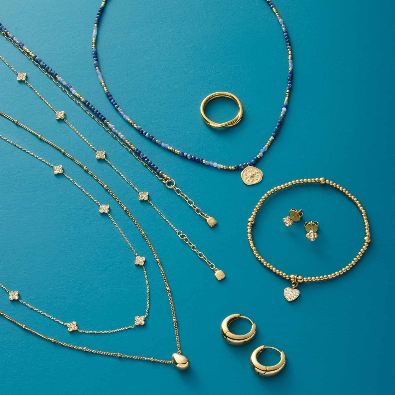 Schmuckkollektion mit Armbändern, Ringen und Halsketten auf türkisblauem Hintergrund