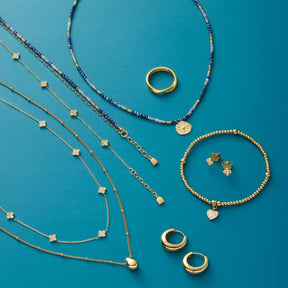 Schmuckkollektion mit Armbändern, Ringen und Halsketten auf türkisblauem Hintergrund