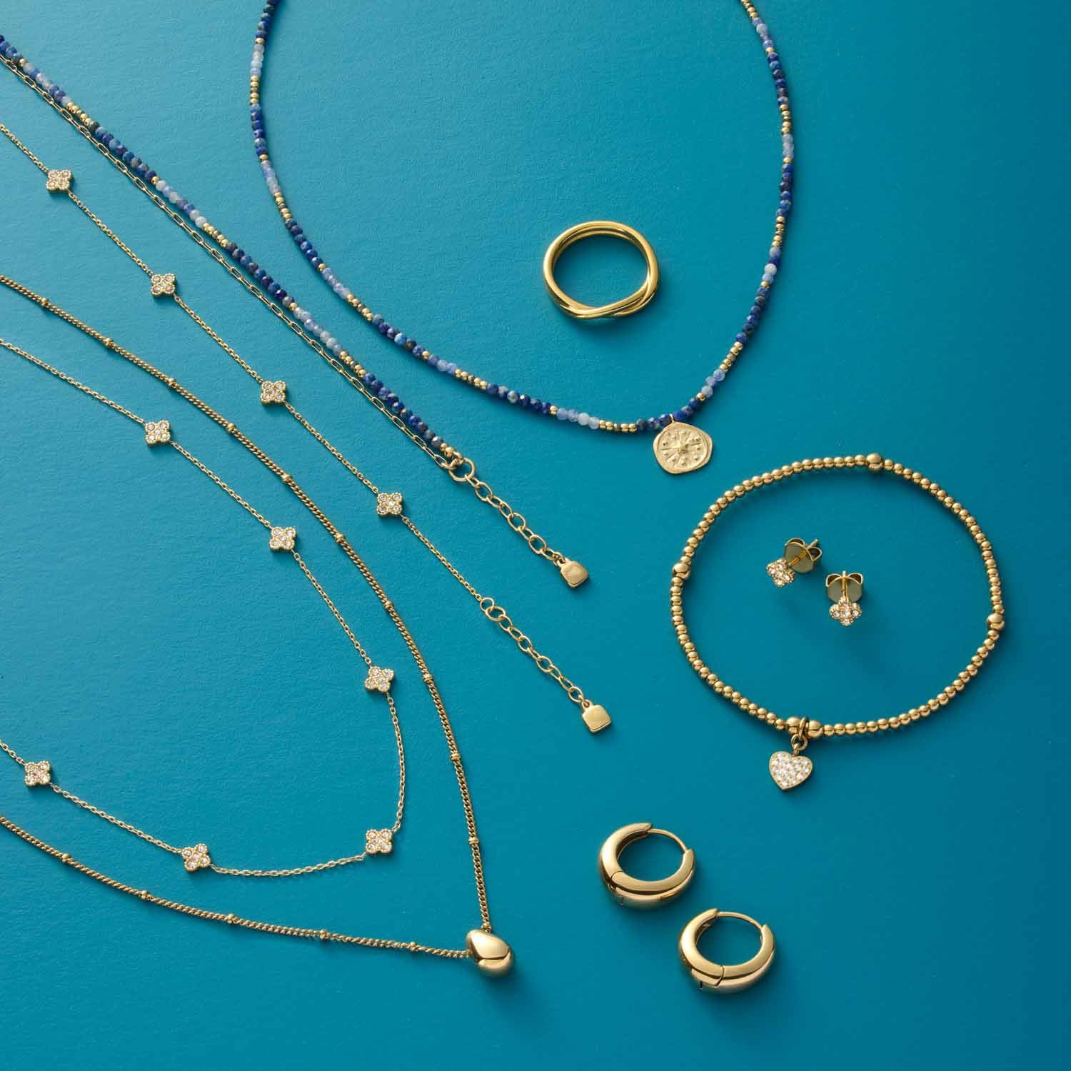 Schmuckkollektion auf blauem Hintergrund: goldene Armbänder, Halsketten, Ringe und Ohrringe