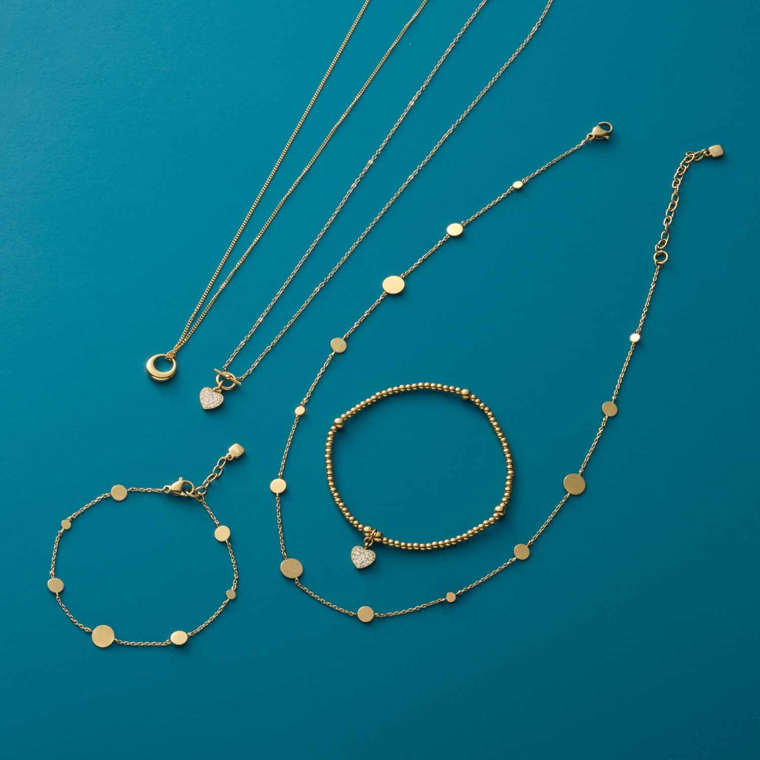 Halskette NOEMI und Armbänder aus der Serie CIAO in Gold auf blauem Hintergrund