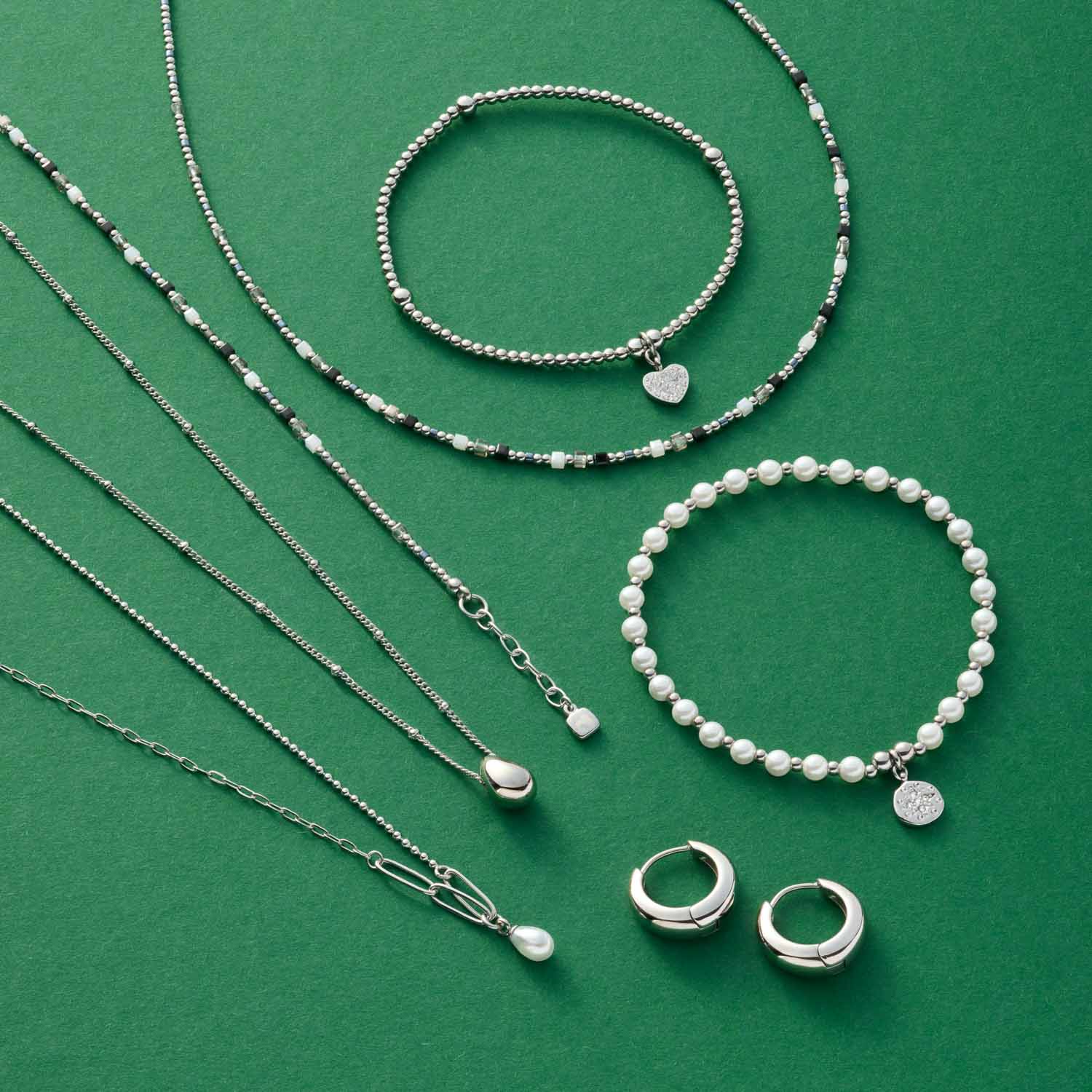Schmuckkollektion aus Halsketten, Armbändern und Ringen auf grünem Hintergrund