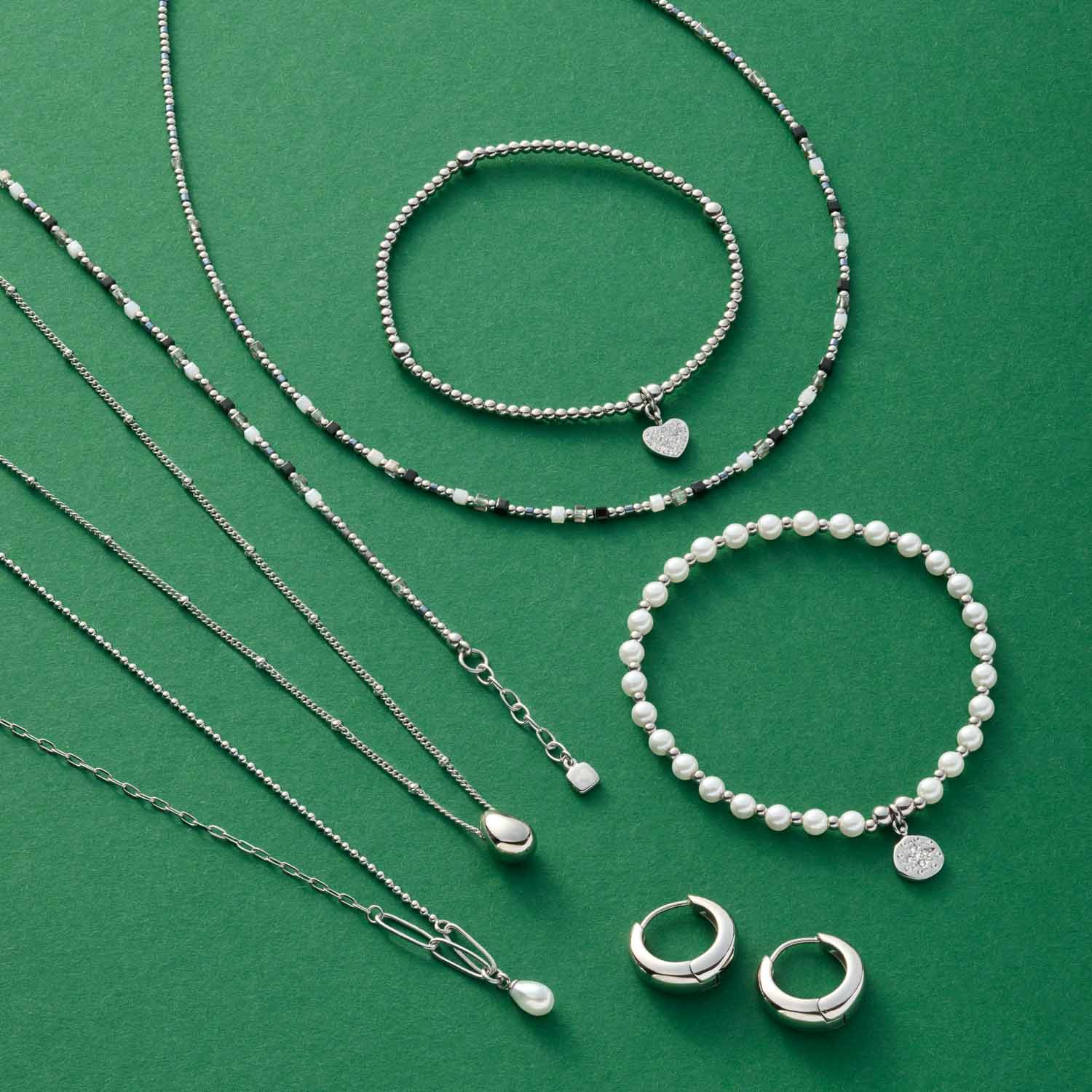 Silberne Creolen, Ketten und Perlenarmbänder auf grünem Hintergrund