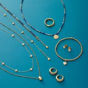 Creole CLOTHILDE gold, Ketten und Armbänder auf blauem Hintergrund arrangiert