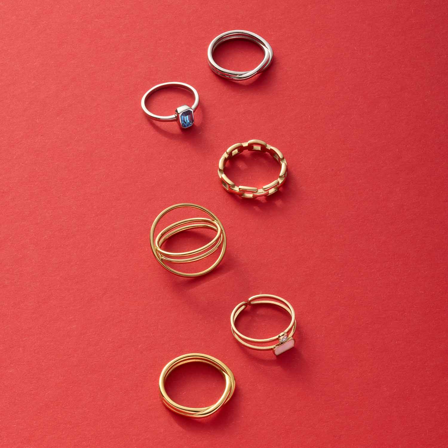 Sechs Ringe aus Silber und Gold auf rotem Hintergrund arrangiert