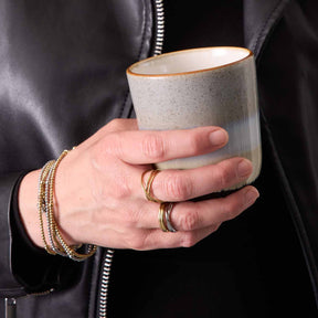 Hand mit goldenen Ringen TWISTER CIAO und Armbändern, hält Keramiktasse