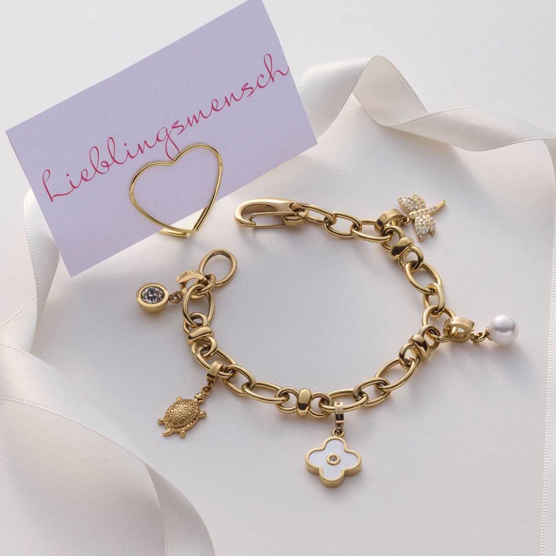Armband VIRGINIA gold mit Charms auf weißem Ribbon und Visitenkarte