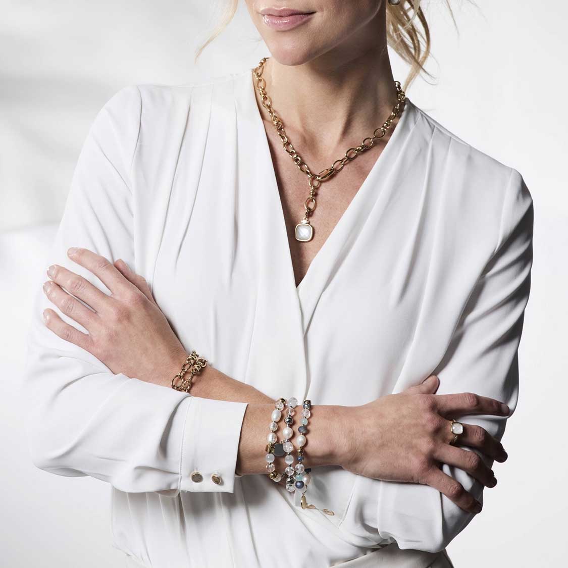 Frau traegt Armband VIRGINIA gold mit Kettengliedern und Perlendetails an Handgelenk