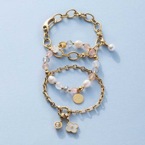 Armband VIRGINIA gold mit Perlen und Charms auf hellblauem Untergrund