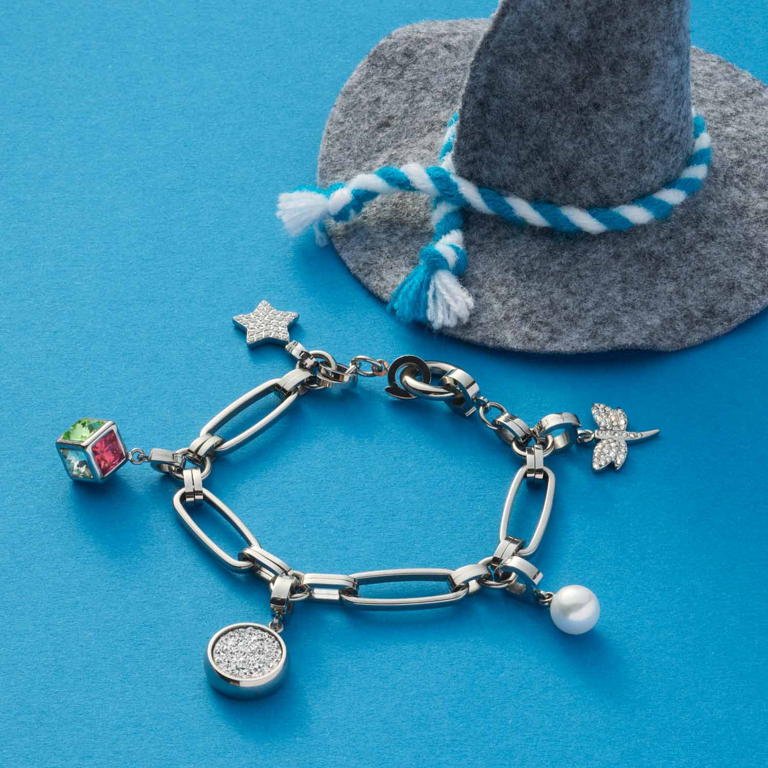 Armband MATHILDE Clip & Mix mit Charms auf blauem Hintergrund neben grauem Hut